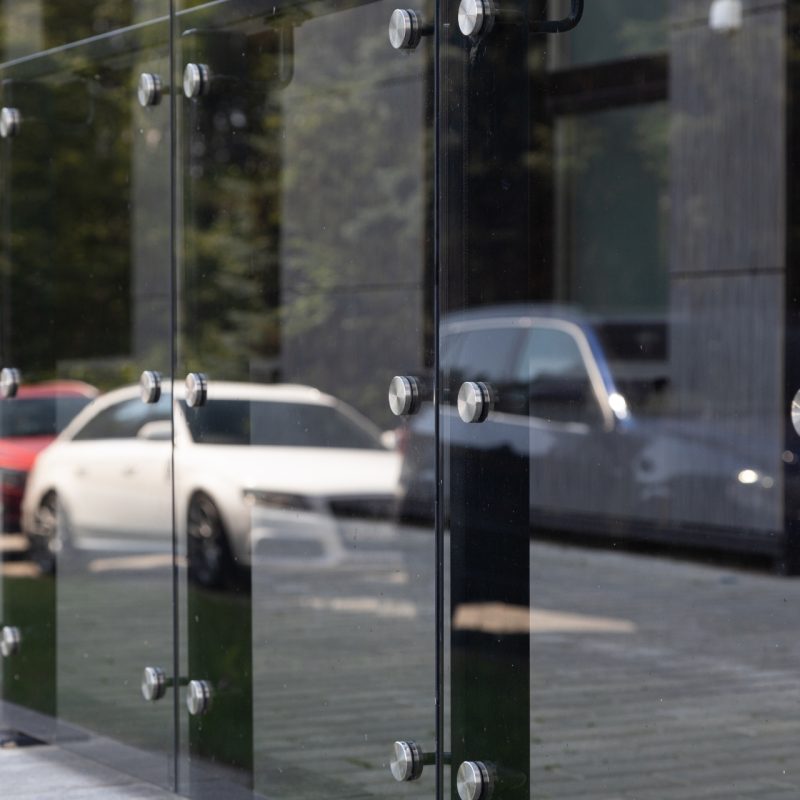 Diagonal view of glass windows or wall with round steel elements with cars and trees reflection on it