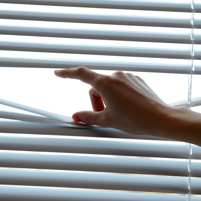 Female hand separating slats of venetian blinds with a finger to see through