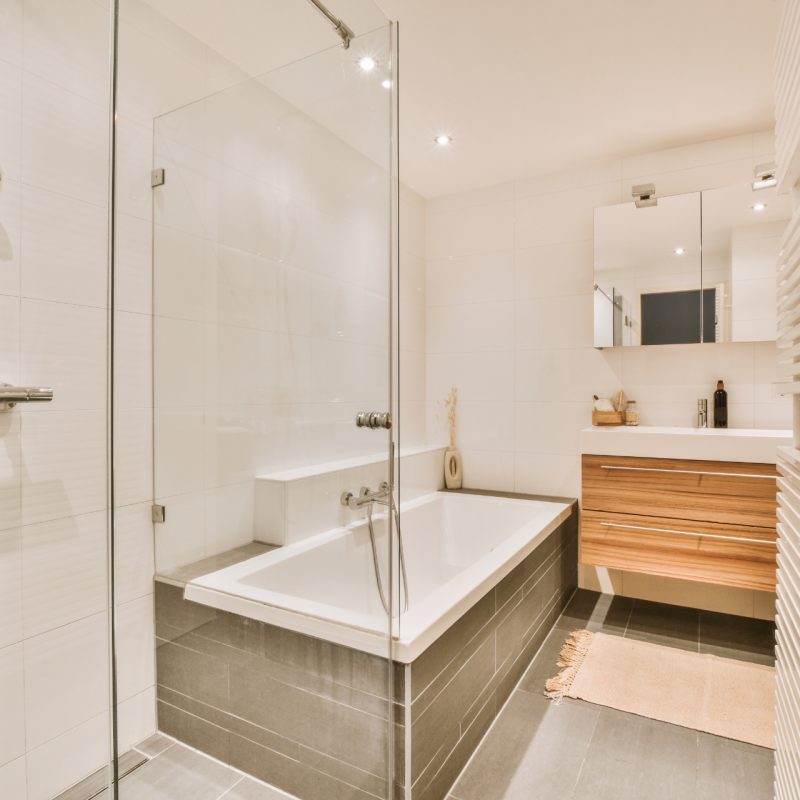 Sinks with mirrors and clean bathtub located near shower box with glass door in modern bathroom with white tiled walls