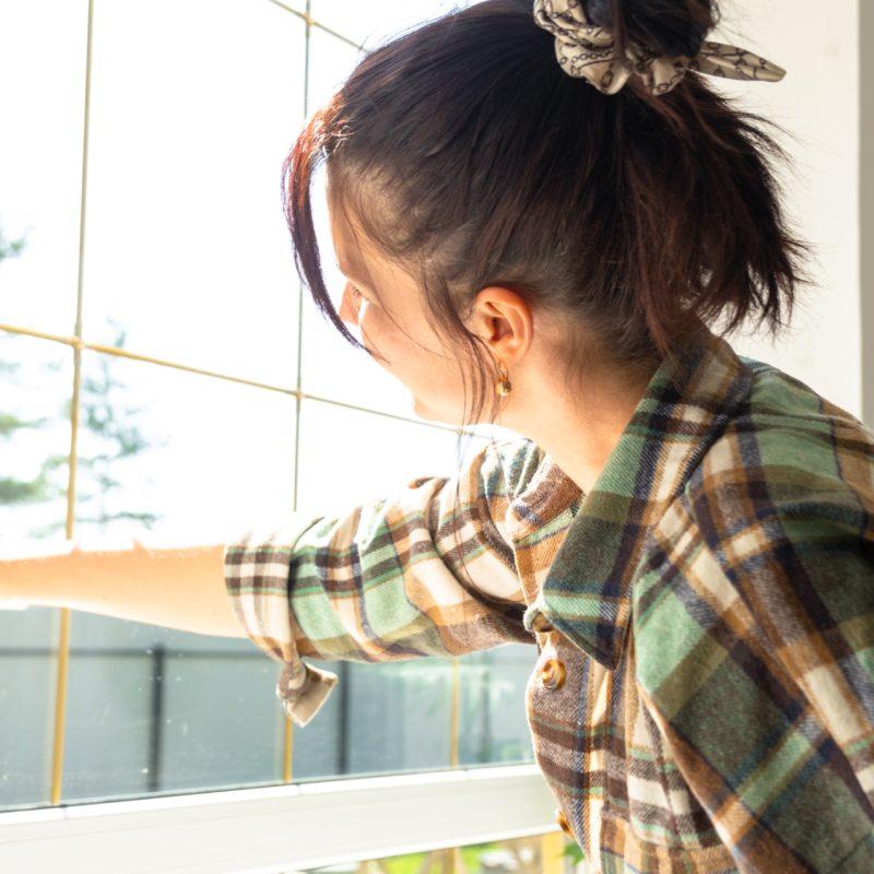 Woman manually washes the window of the house with a rag with spray cleaner and mop inside the interior with white curtains. Restoring order and cleanliness in the spring, cleaning servise